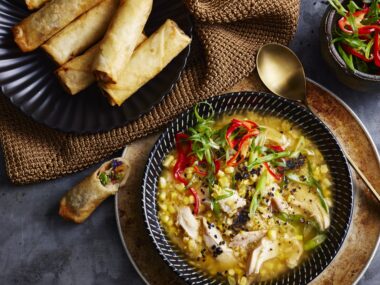 bowl of chicken and corn soup with spring rolls on the side